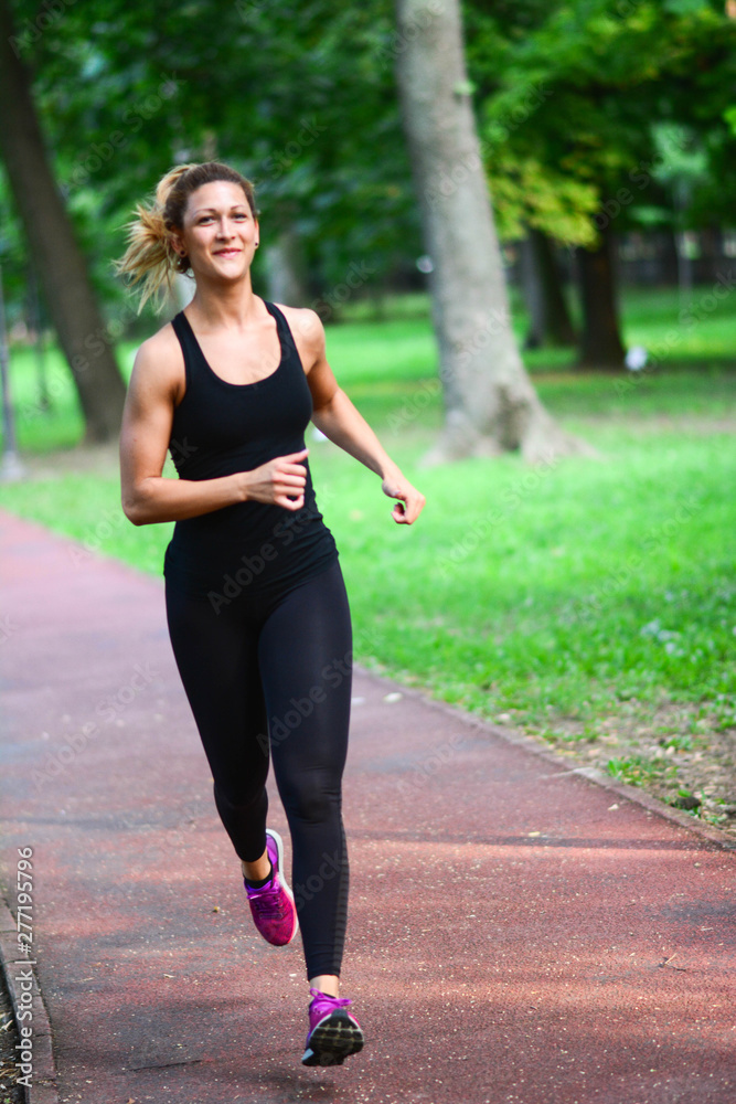 Pretty sporty woman jogging at park in sunrise light. Health conscious concept with copy space. Vertical