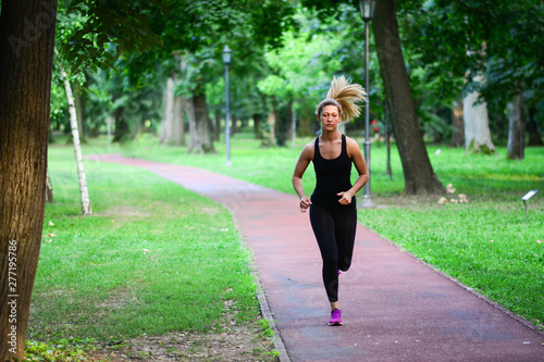 Pretty sporty woman jogging at park in sunrise light. Health conscious concept with copy space.