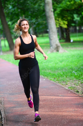 Pretty sporty woman jogging at park in sunrise light. Health conscious concept with copy space. Vertical