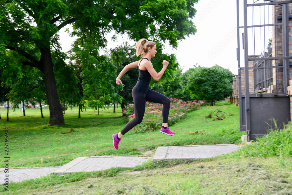 athletic woman working out in park. Fit body. Woman in sportswear sprinting with energy and motion in outdoors nature training cardio with jogging workout exercise.