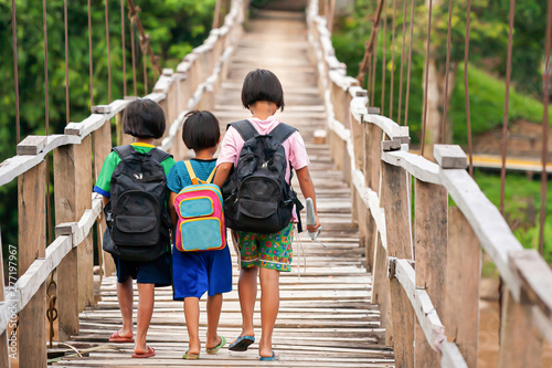 Fotografie Asian primary school girls walking across suspension footbridge at dusk