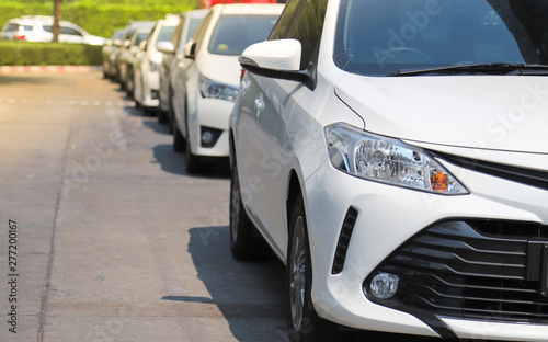 Closeup of front side of white car with  other cars parking in parking lot beside the street in bright sunny day.  © Amphon