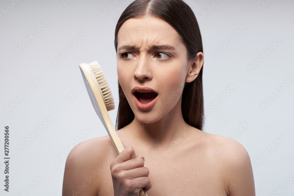 Beautiful young woman with massage brush standing against light blue background Beautiful young woman with massage brush standing against light blue background