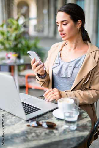 Dreaming attractive girl use mobile phone while sitting with laptop at the cafe,