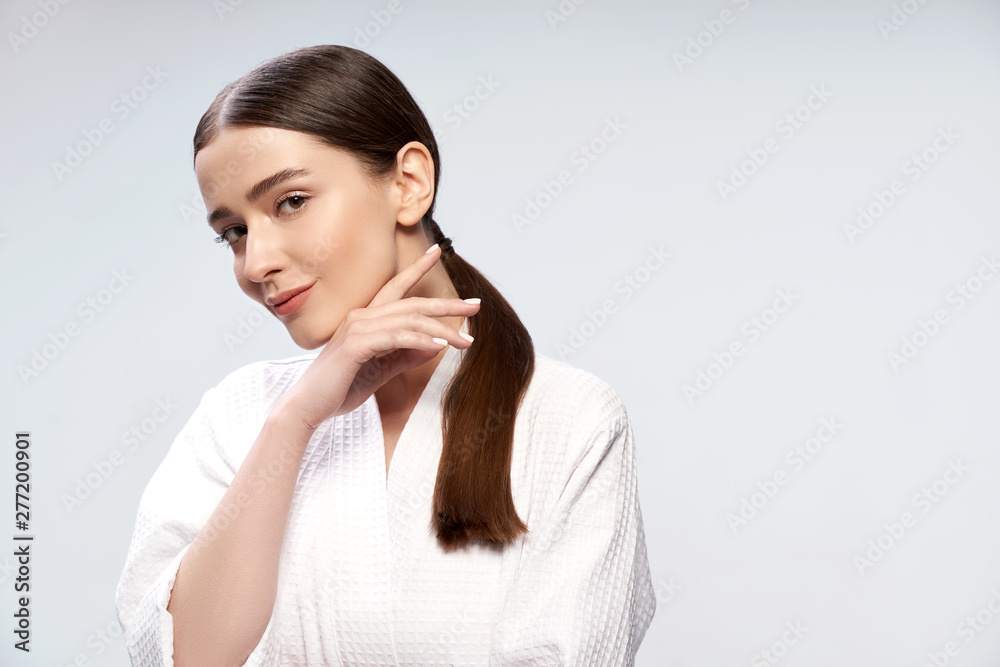 Beautiful young woman in bathrobe standing against light blue background Beautiful young woman in bathrobe standing against light blue background