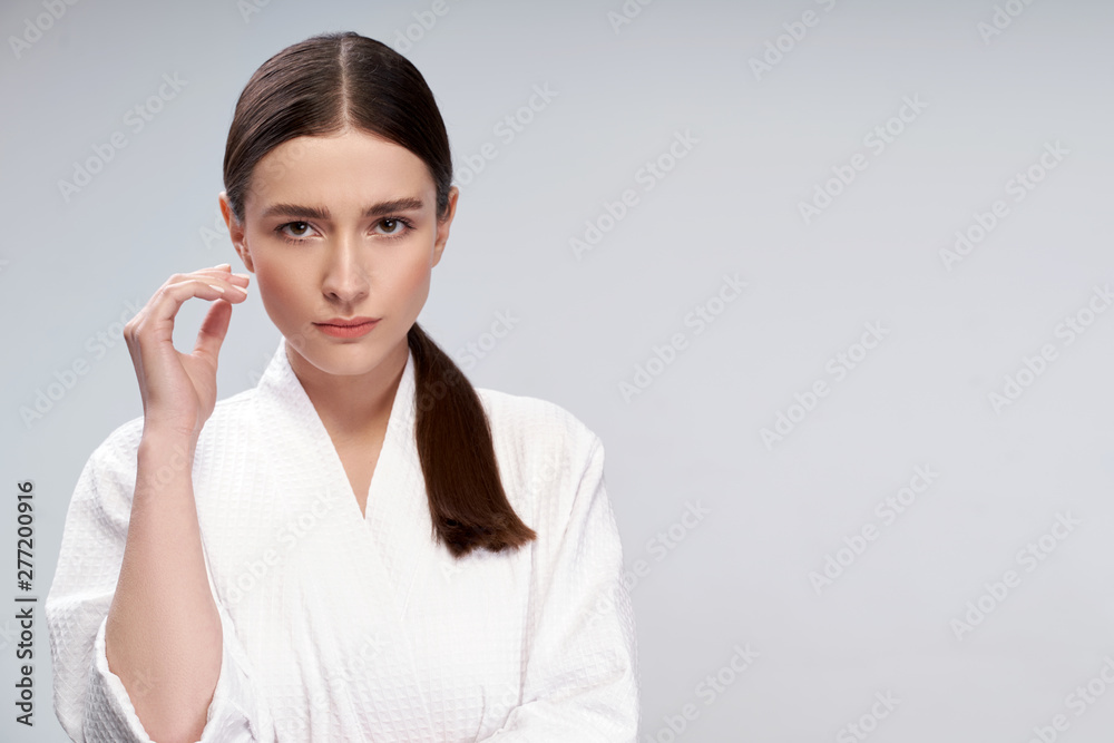Attractive young woman in bathrobe standing against light blue background Attractive young woman in bathrobe standing against light blue background
