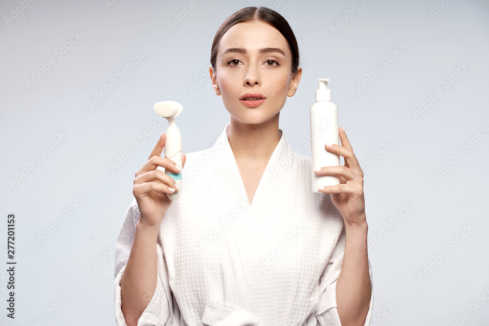 Charming girl holding bottle of cosmetic cream and pore cleansing brush Charming girl holding bottle of cosmetic cream and pore cleansing brush