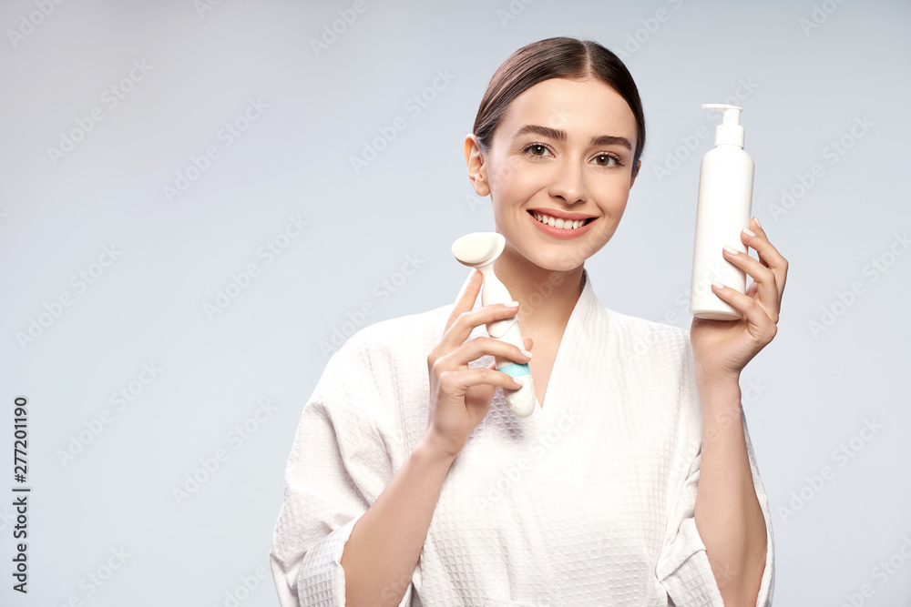 Joyful girl holding bottle of cosmetic cream and pore cleansing brush Joyful girl holding bottle of cosmetic cream and pore cleansing brush