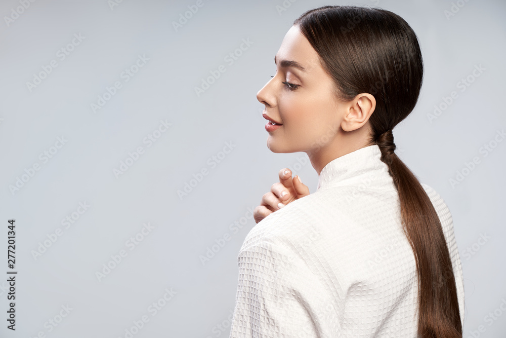 Charming young woman with ponytail standing against light blue background - obrazy, fototapety, plakaty 