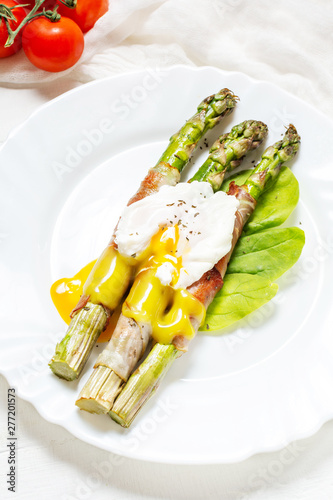 Grilled green asparagus wrapped with bacon, benedict poached egg on white wood background.
