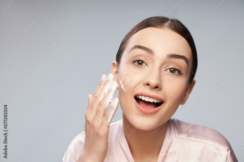 Cheerful young woman washing face with foaming cleanser Cheerful young woman washing face with foaming cleanser