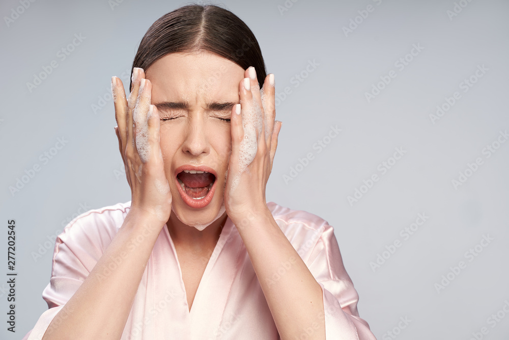 Young woman with purifying foam on face closing eyes and screaming Young woman with purifying foam on face closing eyes and screaming