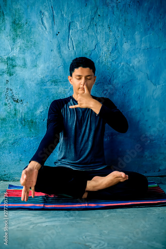 Portrait shot of the young man doing pranayama or pranayam or breath control yoga on a colorful mat with wearing black attire.