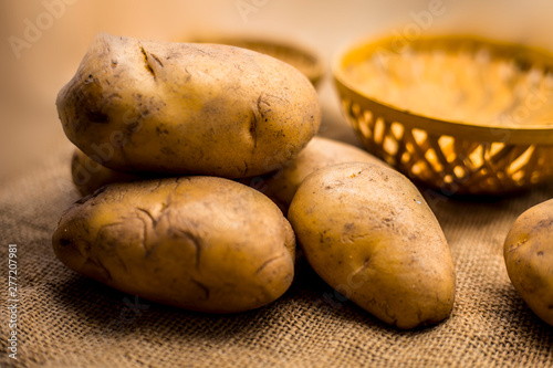 Close up shot of potato or aloo or alu on jute bag surface along with two vegetable and fruit hampers.