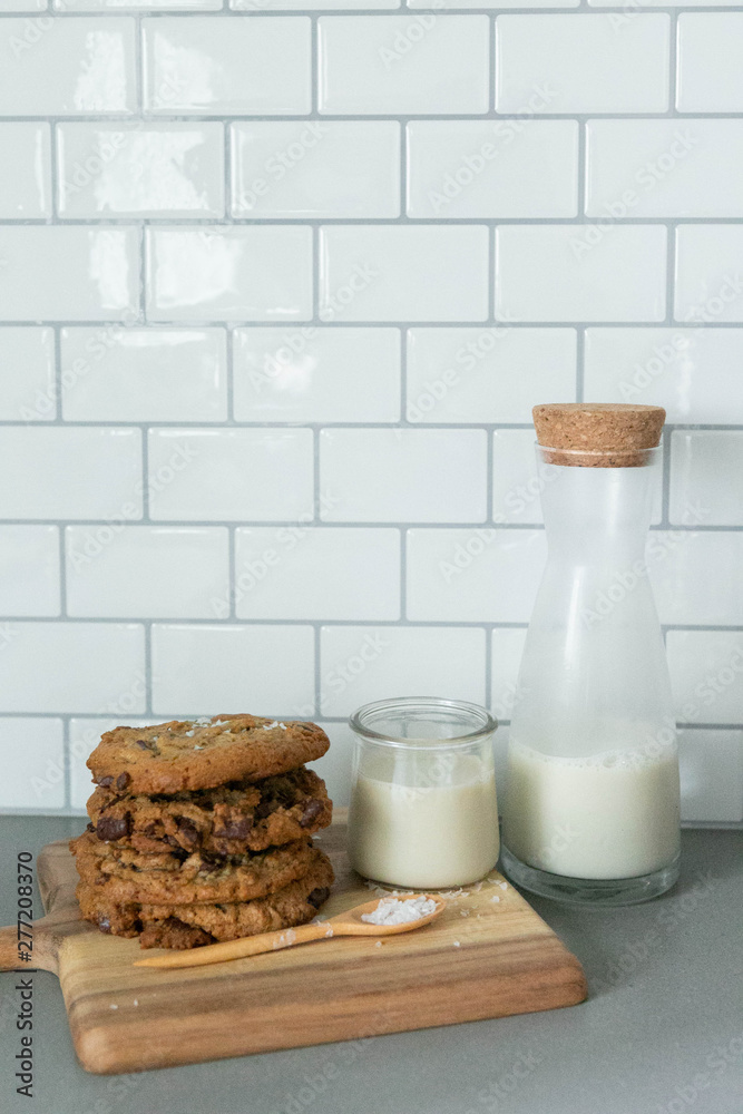 Stack of Homemade Salted Chocolate Chip Cookies with glass of milk, White Subway Tile Background, Wooden Plate