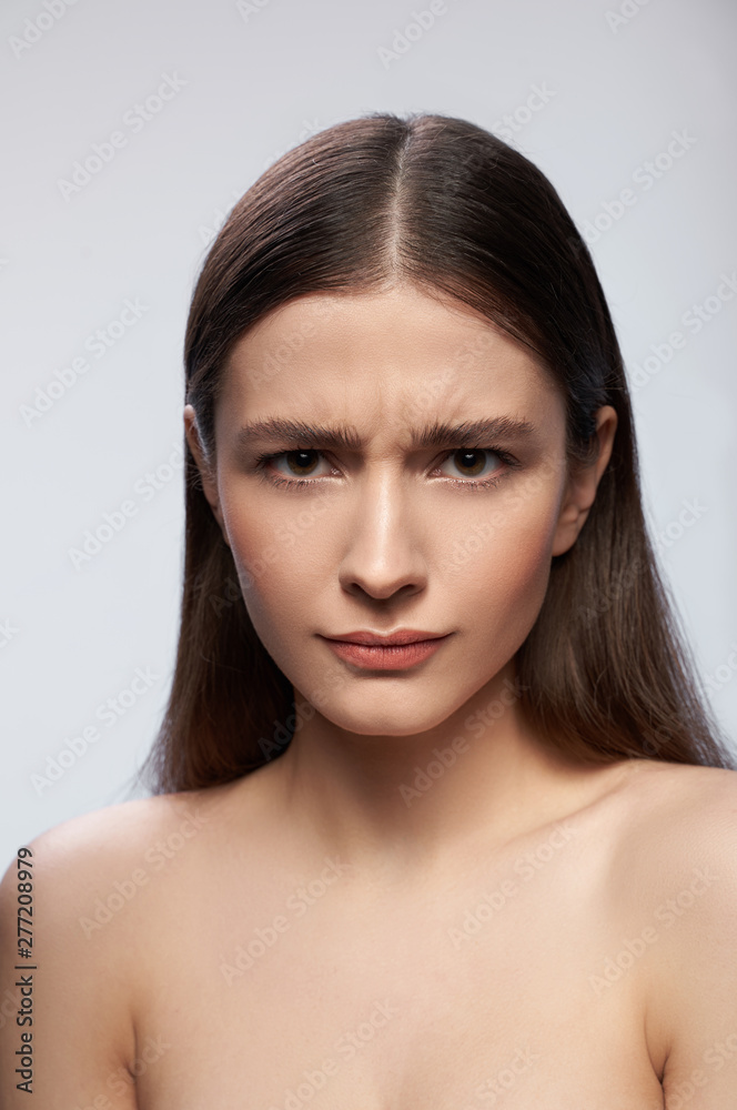 Frowning lady standing against light gray background in studio Frowning lady standing against light gray background in studio