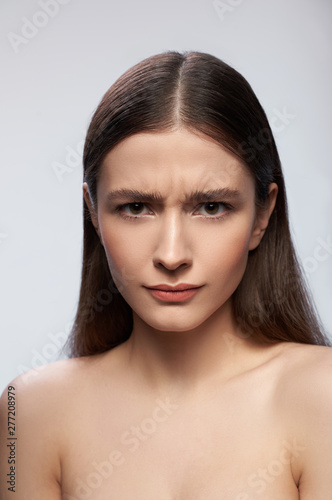 Frowning lady standing against light gray background in studio