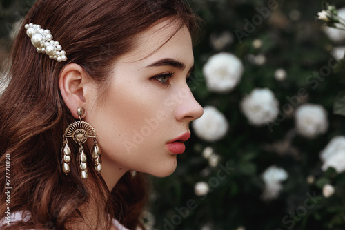 Outdoor close up portrait of young fashionable lady wearing trendy vintage style earrings, white pearl barrette in the long hair. Copy, empty space for text  photo