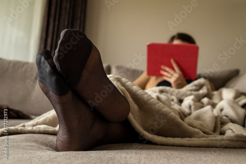 Foto A portrait of crossed feet in pantyhose of a woman relaxing using her tablet in the couch under a blanket at home to relax