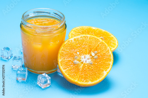 Glass of orange juice with sliced orange fruit and ice cubes on blue background