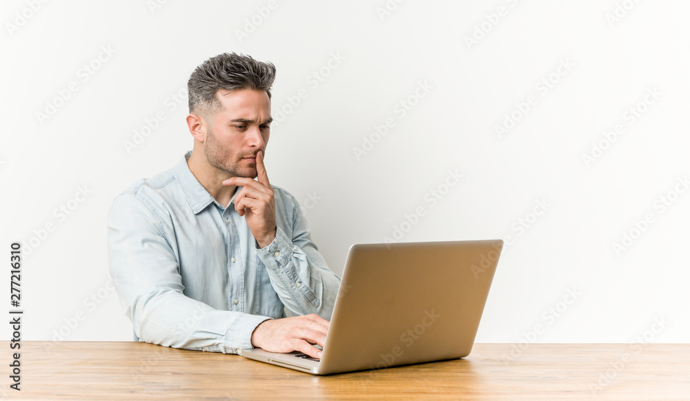 Young handsome man working with his laptop looking sideways with doubtful and skeptical expression. Young handsome man working with his laptop looking sideways with doubtful and skeptical expression.
