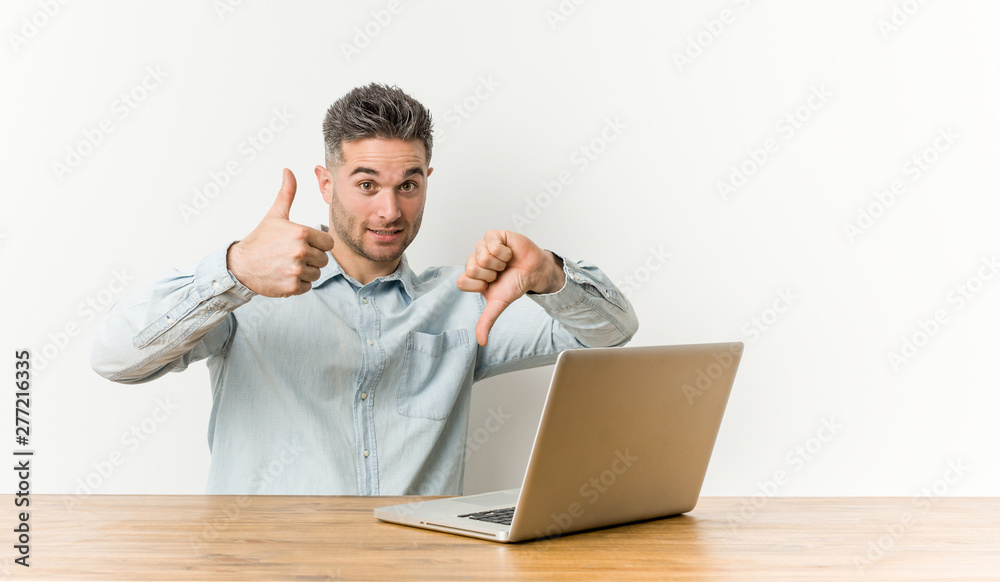 Young handsome man working with his laptop showing thumbs up and thumbs down, difficult choose concept