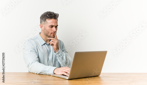 Young handsome man working with his laptop looking sideways with doubtful and skeptical expression.