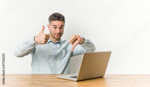 Young handsome man working with his laptop showing thumbs up and thumbs down, difficult choose concept