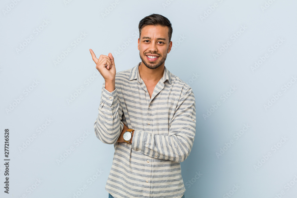 Young handsome filipino man smiling cheerfully pointing with forefinger away. Young handsome filipino man smiling cheerfully pointing with forefinger away.