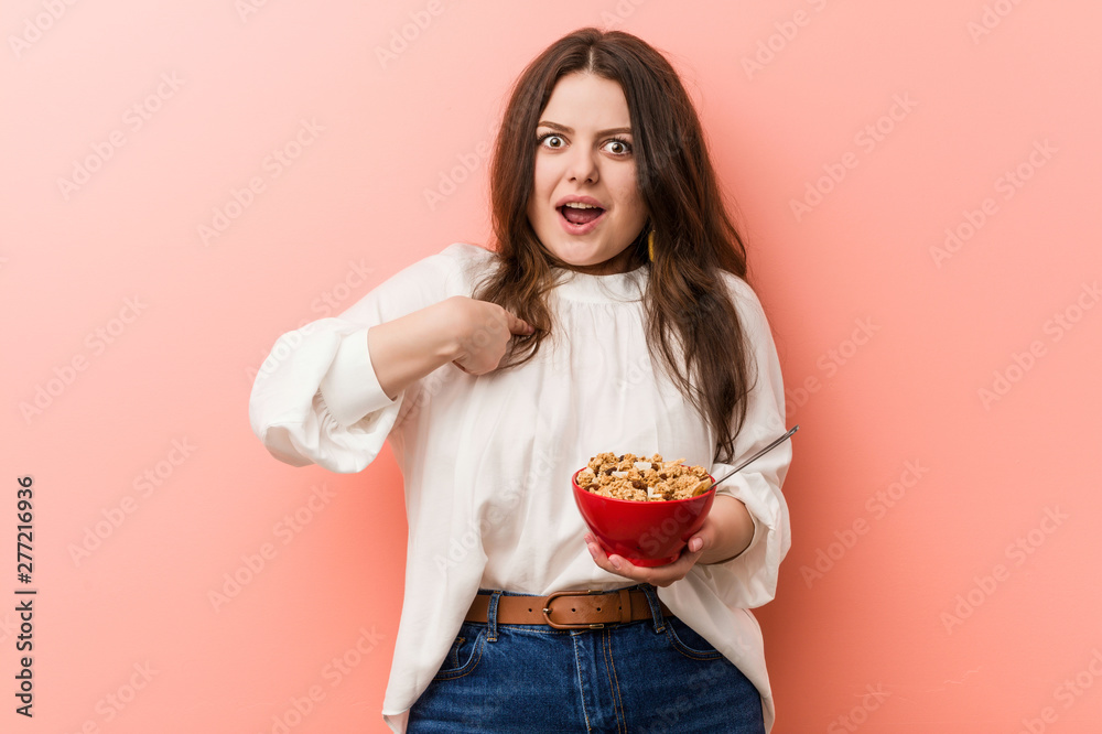 Young plus size curvy woman holding a cereals bowl surprised pointing at himself, smiling broadly. Young plus size curvy woman holding a cereals bowl surprised pointing at himself, smiling broadly.