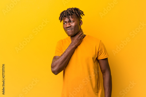 Young black man wearing rastas over yellow background suffers pain in throat due a virus or infection.