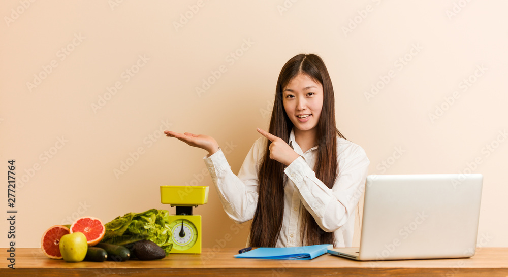 Young nutritionist chinese woman working with her laptop excited holding a copy space on palm. Young nutritionist chinese woman working with her laptop excited holding a copy space on palm.