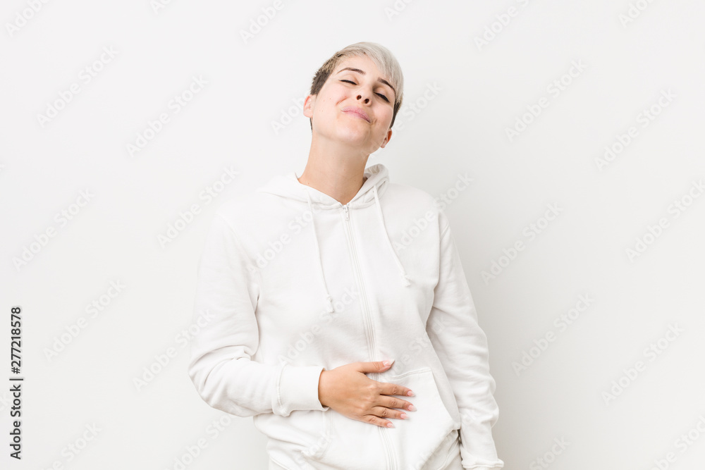 Young curvy woman wearing a white hoodie touches tummy, smiles gently, eating and satisfaction concept. Young curvy woman wearing a white hoodie touches tummy, smiles gently, eating and satisfaction concept.