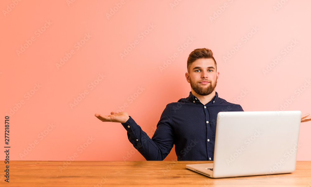 Young man working with his laptop makes scale with arms, feels happy and confident. Young man working with his laptop makes scale with arms, feels happy and confident.