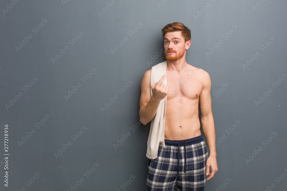 Young redhead man holding a towel inviting to come. He is holding a white towel.