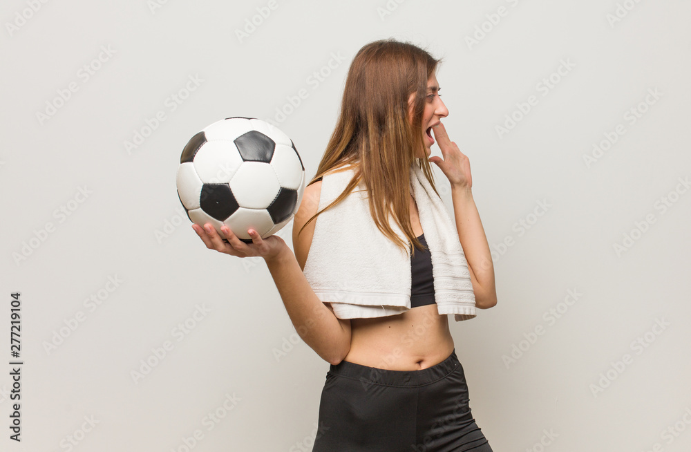 Young fitness russian woman whispering gossip undertone. Holding a soccer ball.