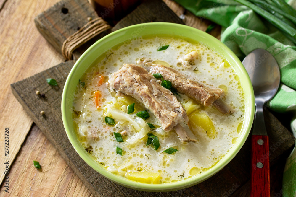 Vegetable soup with cabbage, sour cream and meat ribs on a kitchen wooden table. Free space for your text. Vegetable soup with cabbage, sour cream and meat ribs on a kitchen wooden table. Free space for your text.