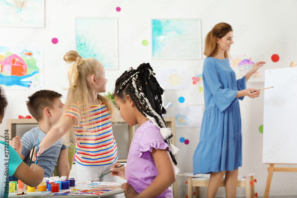 Children with female teacher at painting lesson indoors - obrazy, fototapety, plakaty 