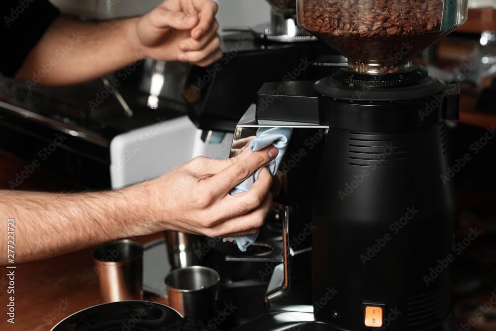 Barista cleaning coffee grinding machine with rag in cafe, closeup Barista cleaning coffee grinding machine with rag in cafe, closeup