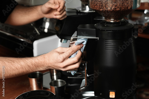 Barista cleaning coffee grinding machine with rag in cafe, closeup