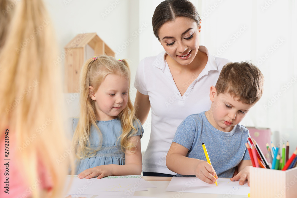 Little children with kindergarten teacher drawing at table indoors. Learning and playing Little children with kindergarten teacher drawing at table indoors. Learning and playing