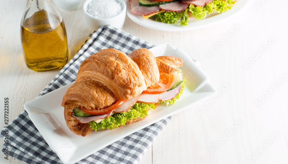 Fresh croissant or sandwich with salad, ham, jamon, prosciutto, salami, cheese, chicken, tomatoes on wooden background. Morning breakfast concept. Healthy and fast food. Fresh croissant or sandwich with salad, ham, jamon, prosciutto, salami, cheese, chicken, tomatoes on wooden background. Morning breakfast concept. Healthy and fast food.