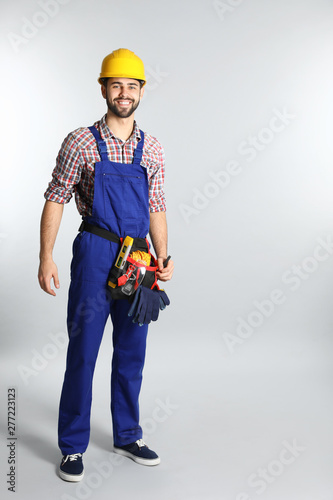 Full length portrait of construction worker with tool belt on light background. Space for text