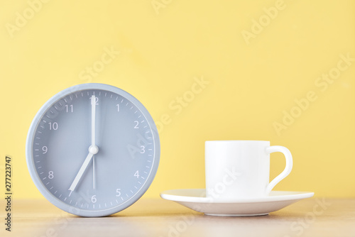 Classic gray alarm clock and white coffee cup on a yellow background