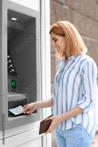 Beautiful woman taking money from cash machine outdoors