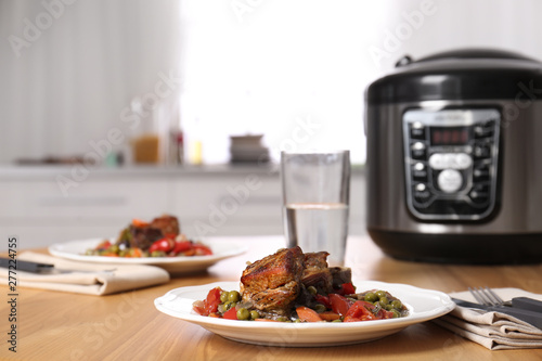 Plate with meat and garnish prepared in multi cooker on wooden table in kitchen. Space for text