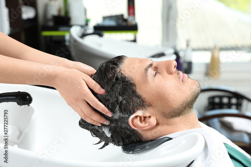 Stylist washing client's hair at sink in beauty salon