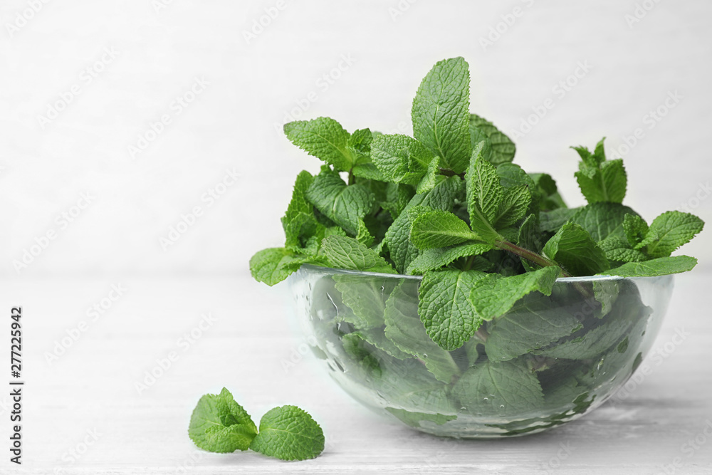 Glass bowl with fresh green mint on table. Space for text