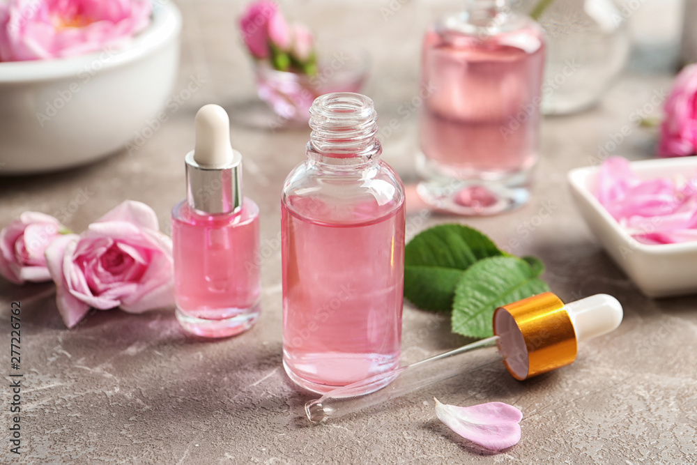 Bottles of rose essential oil, pipette and flowers on table Bottles of rose essential oil, pipette and flowers on table
