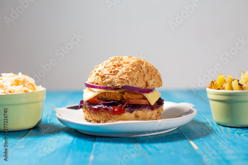 Delicious homemade burger with french fries and salad (coul slow) on a blue table and neutral grey background
